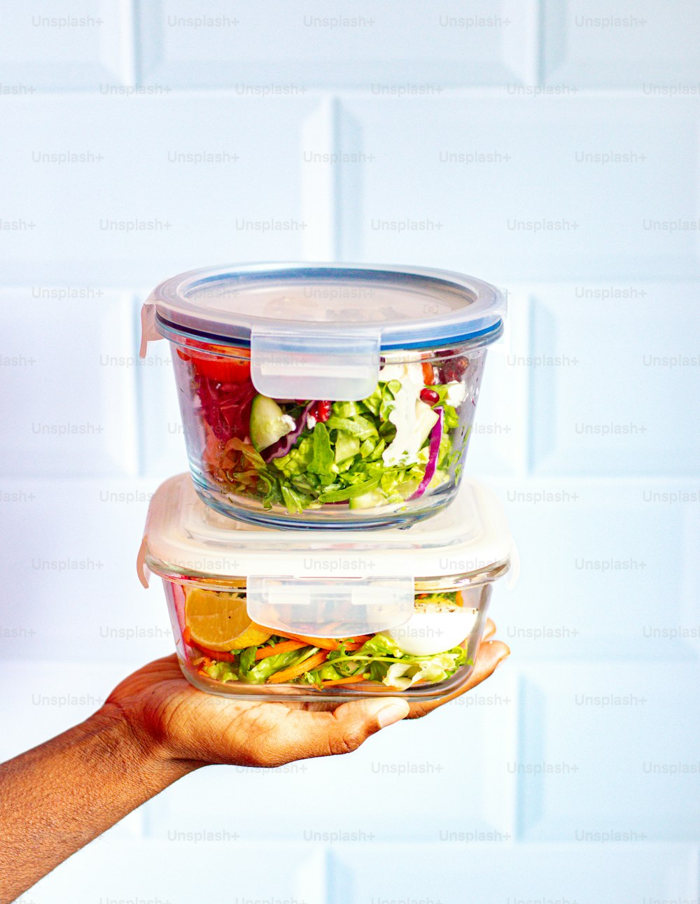 a person holding two plastic containers filled with food