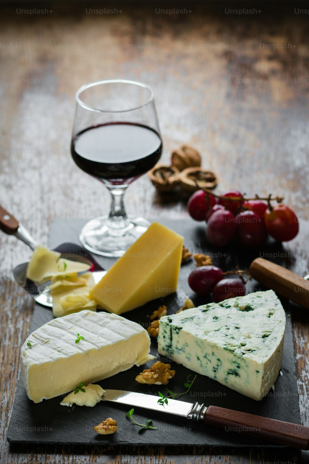 uma taça de vinho, queijo, nozes e bolachas em uma mesa de madeira