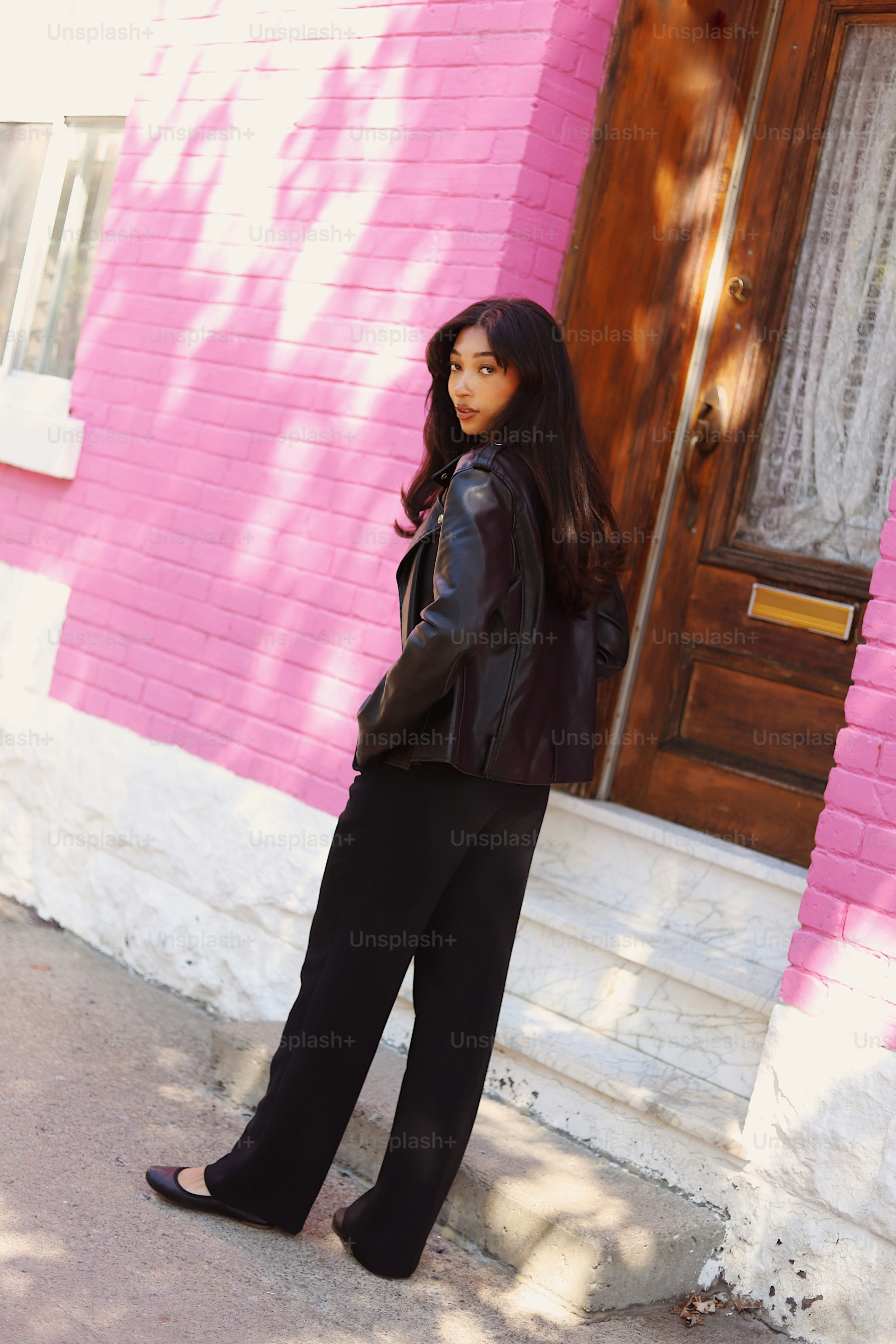 A woman standing in front of a pink building photo – Fashion Image on ...