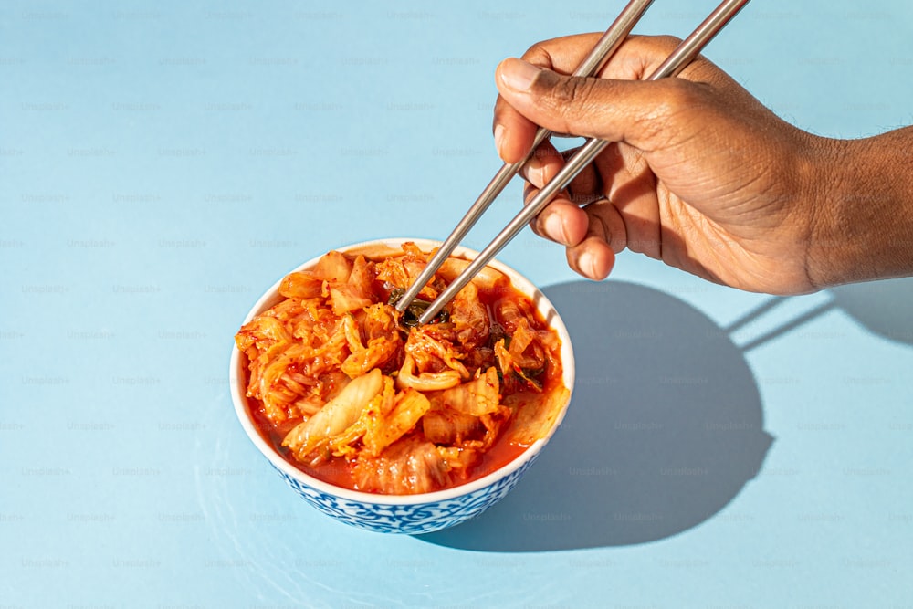 a person holding chopsticks over a bowl of food