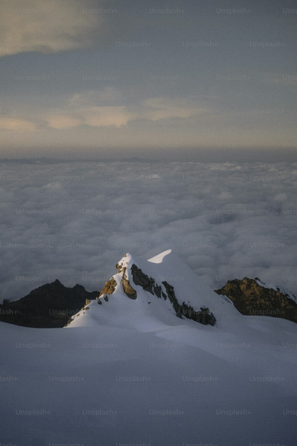 a mountain covered in snow and clouds under a cloudy sky