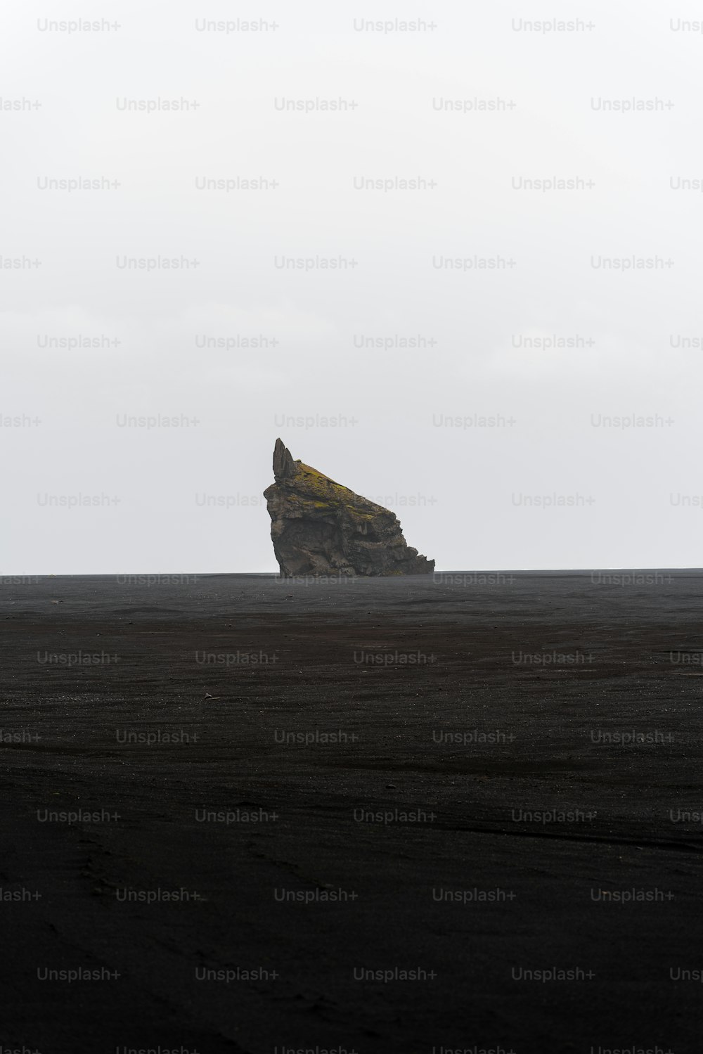 검은 해변 위에 앉아있는 큰 바위