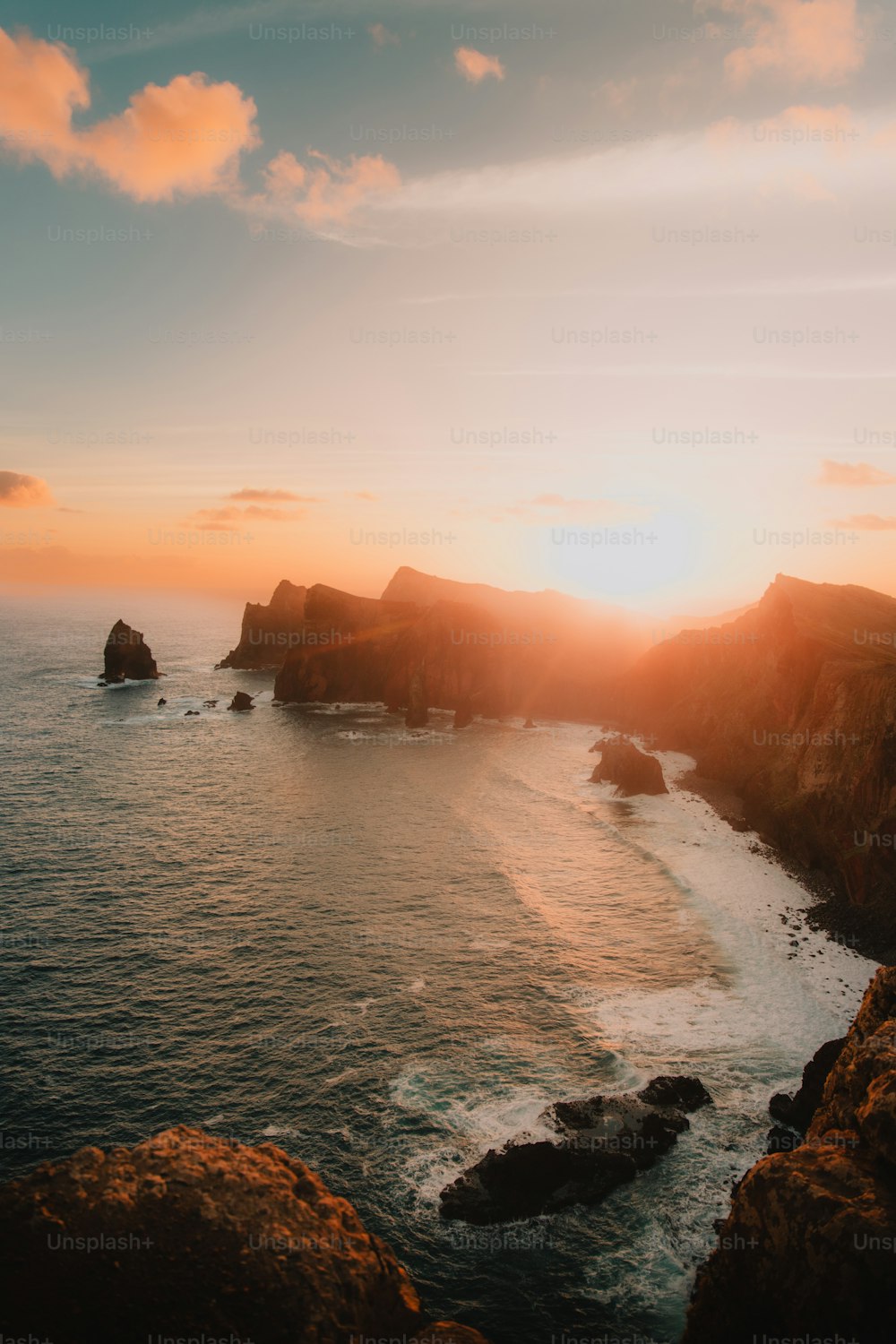 the sun is setting over the ocean near a rocky shore