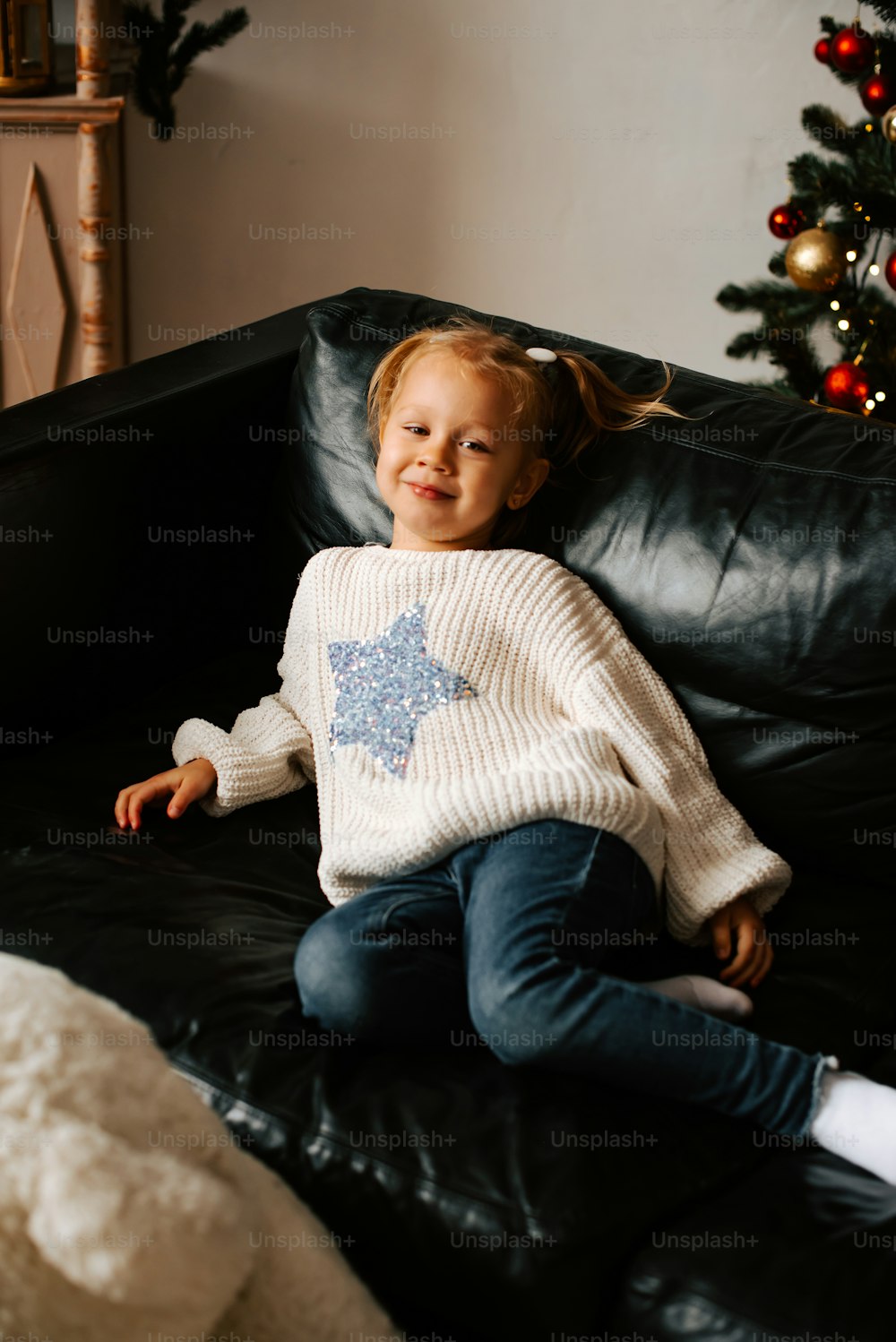 a little girl sitting on a couch in front of a christmas tree