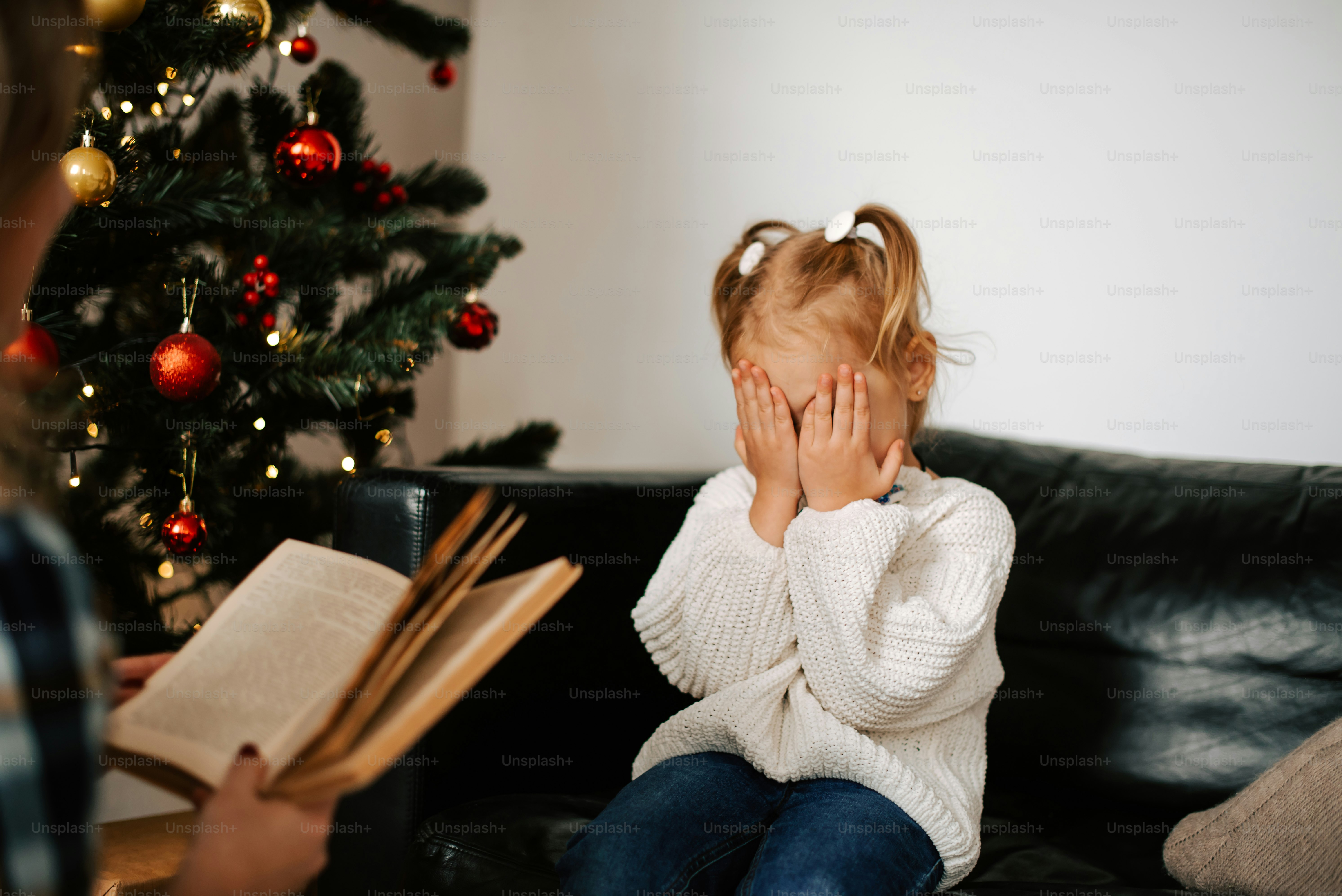 a little girl sitting on a couch holding her hands to her face