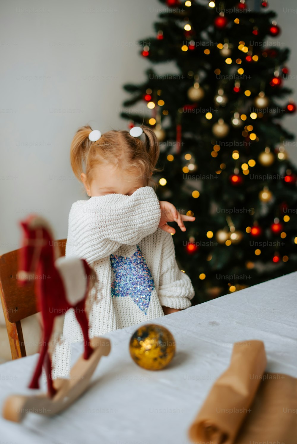 a little girl sitting at a table in front of a christmas tree