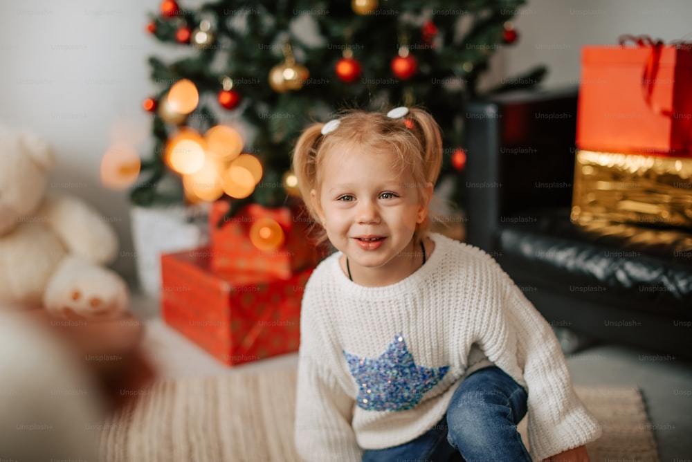 a little girl sitting in front of a christmas tree