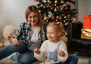 a woman sitting next to a little girl in front of a christmas tree