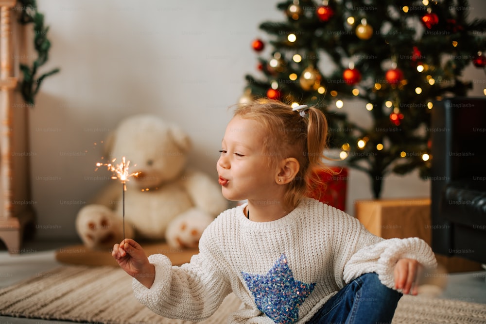 a little girl sitting on the floor holding a sparkler
