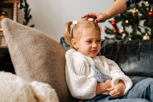 a little girl sitting on a couch with a christmas tree in the background