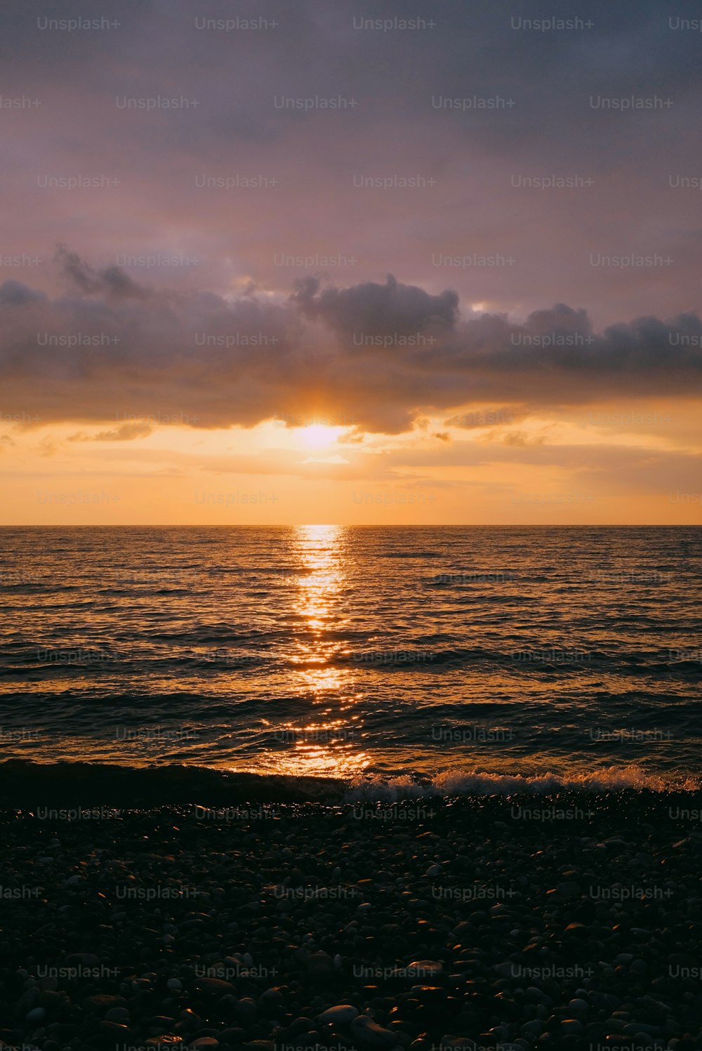 the sun is setting over the ocean on a cloudy day