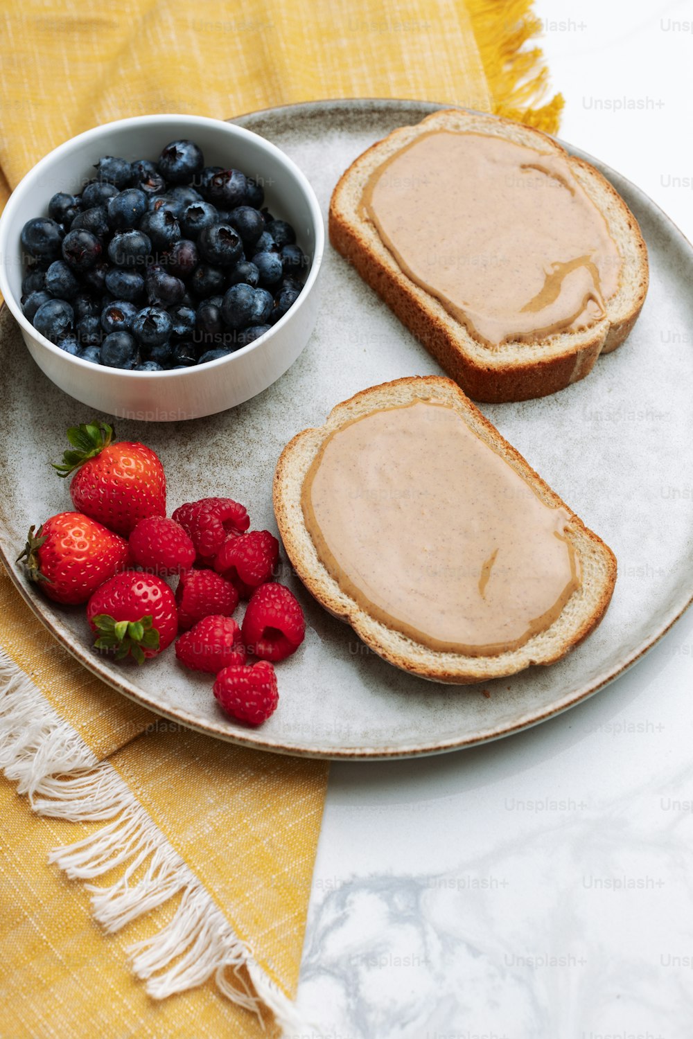 a plate of toast, berries and a bowl of peanut butter