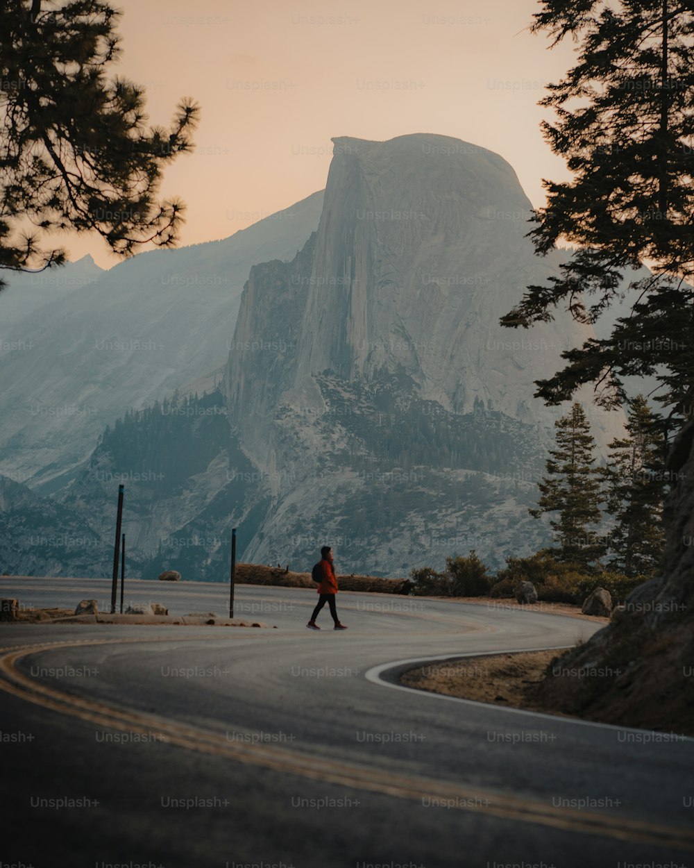 a person walking down a road in front of a mountain