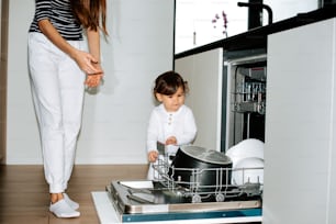 a little girl standing in front of a dishwasher