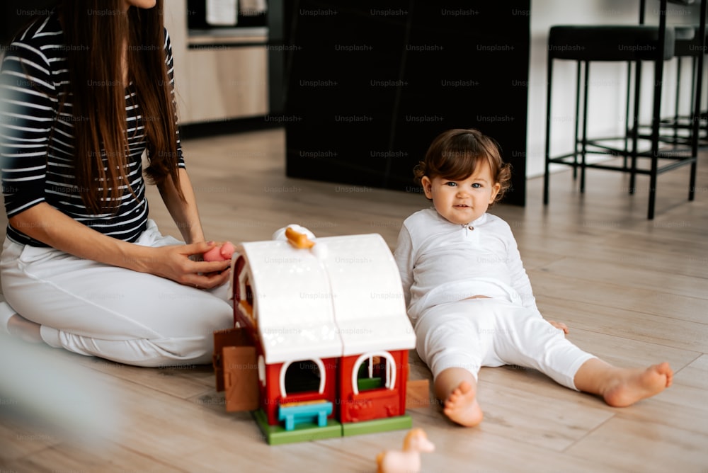 a woman sitting on the floor with a baby next to a toy house