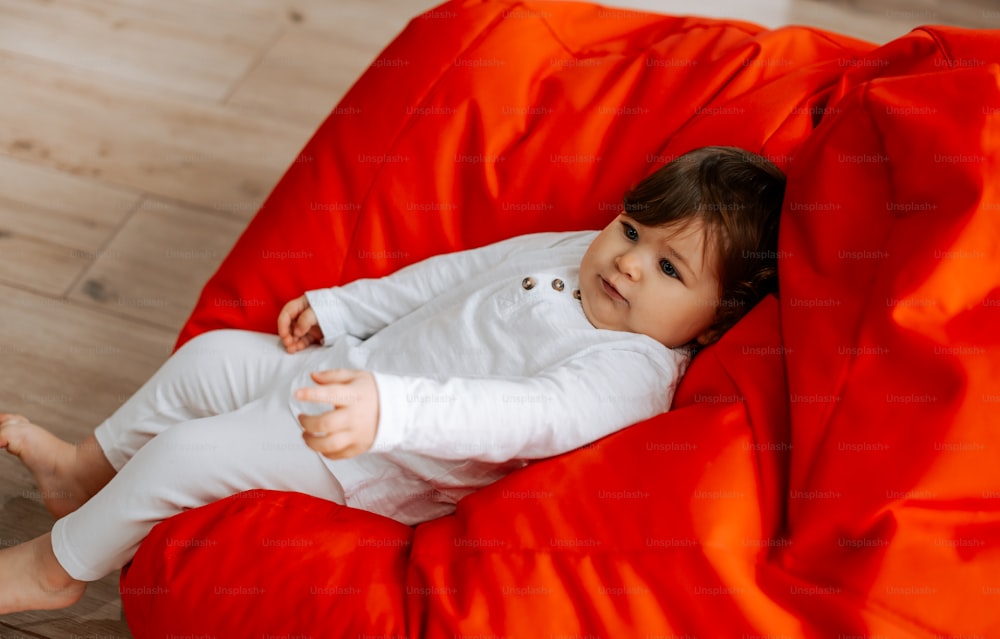 a baby sitting on a red bean bag chair