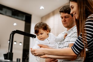 a man and woman holding a baby in front of a faucet