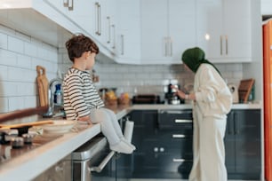 a little boy sitting on a kitchen counter next to a woman