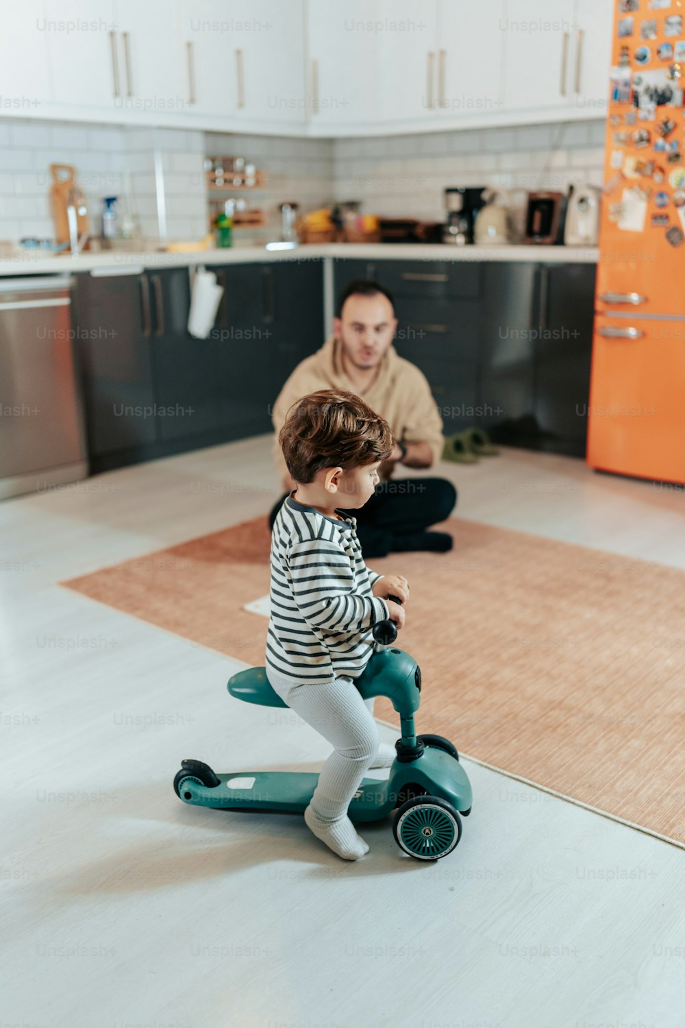 a man and a little girl riding a scooter in a kitchen