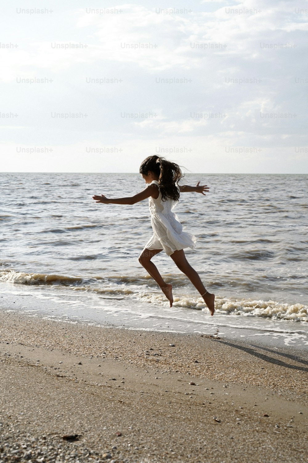 ein kleines Mädchen, das am Strand in die Luft springt