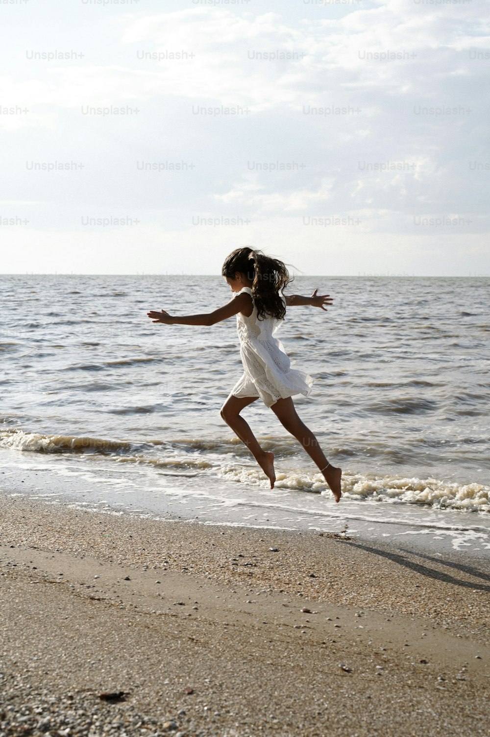 a little girl jumping in the air on a beach