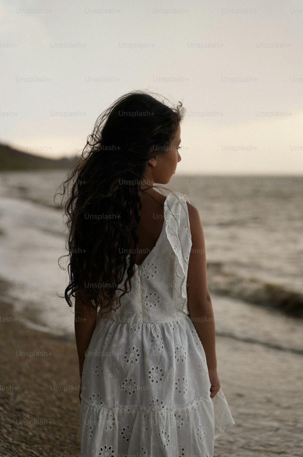 a girl in a white dress walking on the beach