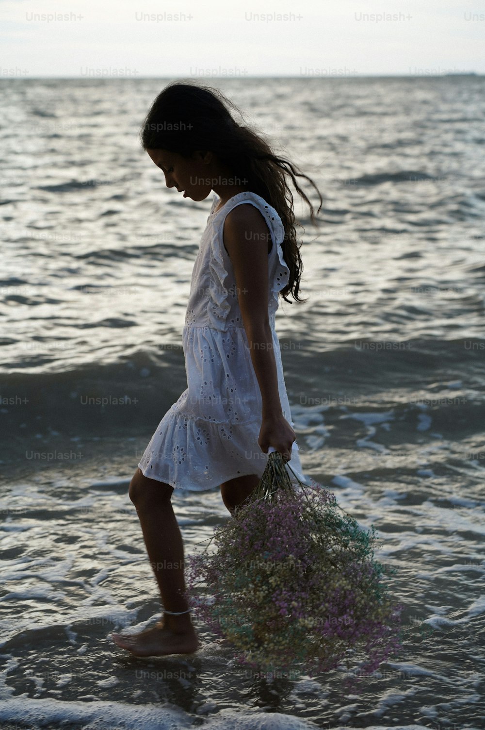 a young girl walking into the ocean holding a bouquet of flowers