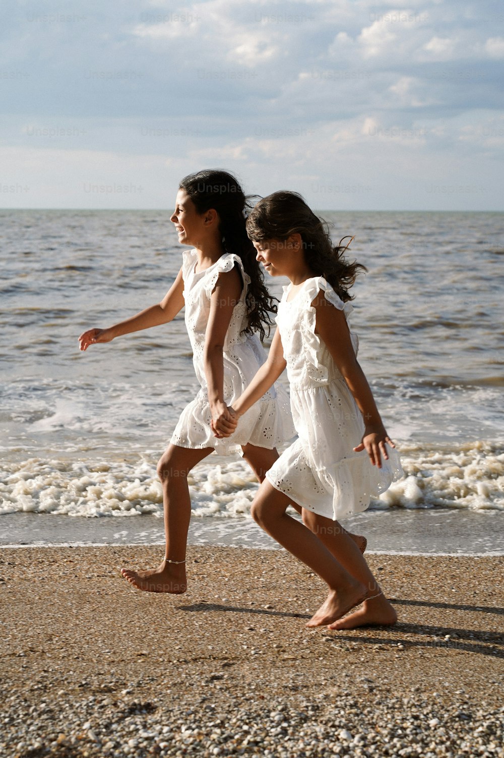 two young girls are walking on the beach