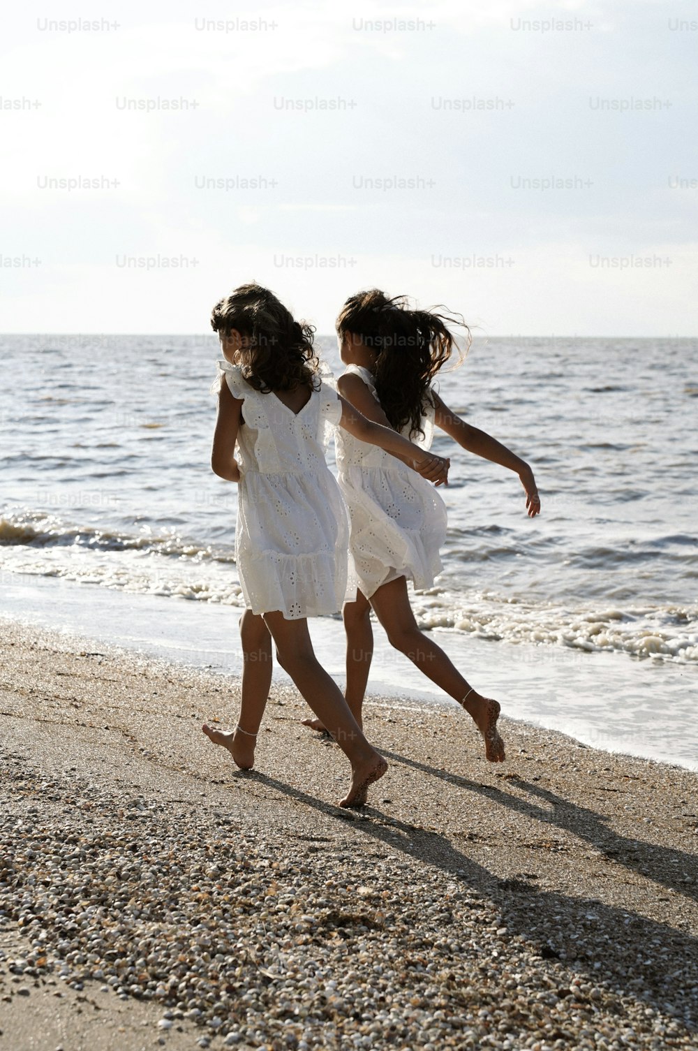 두 명의 어린 소녀가 해변을 따라 물을 향해 달립니다
