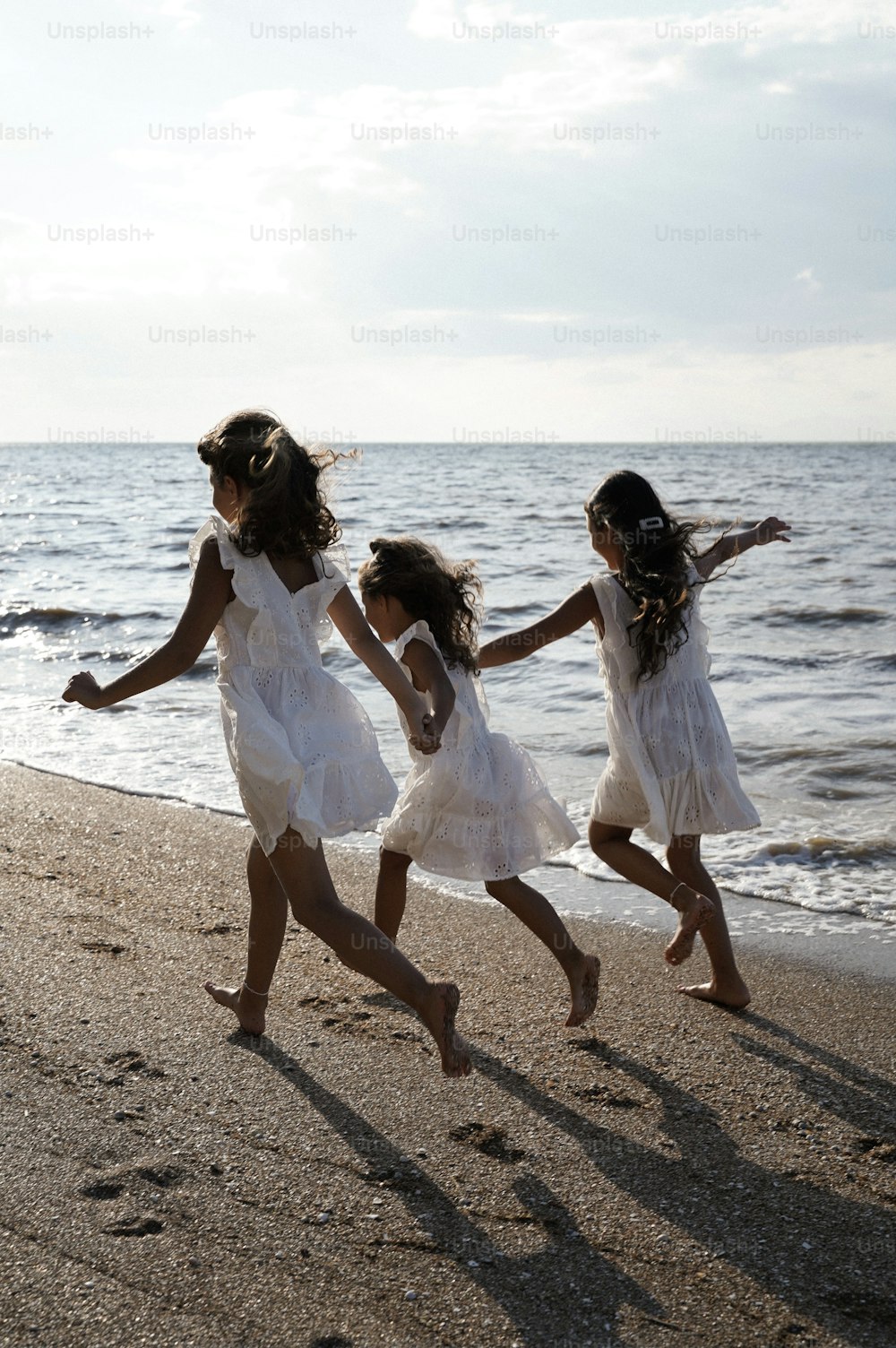해변에서 함께 달리는 세 명의 어린 소녀