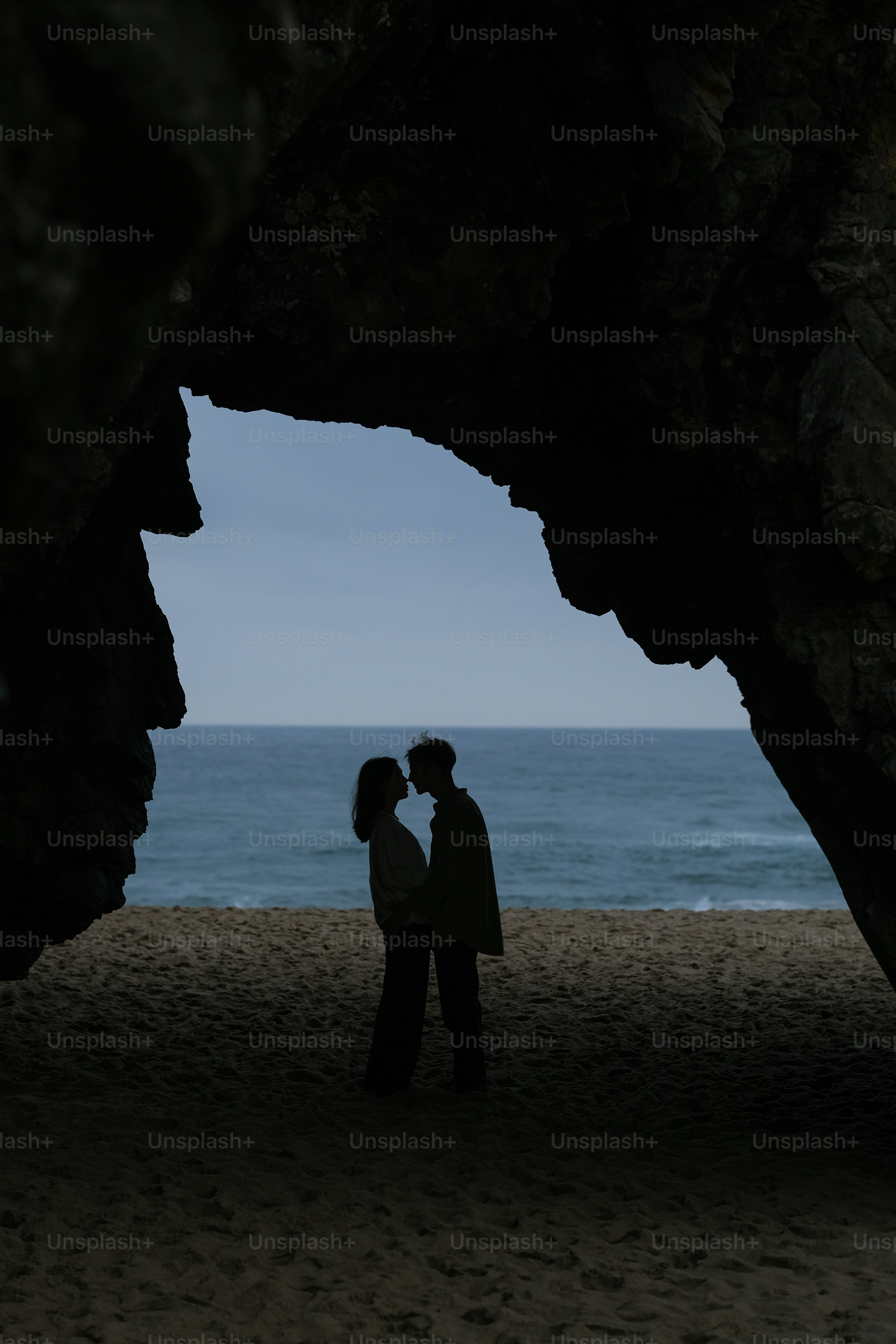 a man and a woman standing under a cave on a beach