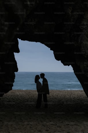 a man and a woman standing under a cave on a beach