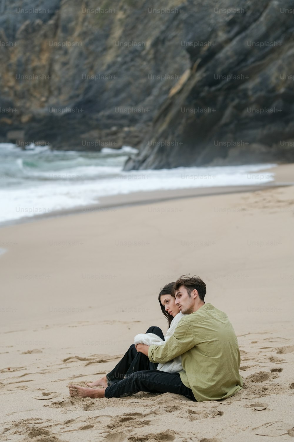 a man and woman sitting on a beach next to the ocean