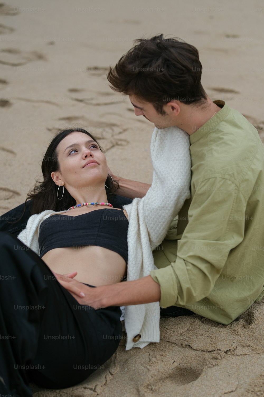 a man sitting next to a pregnant woman on a beach