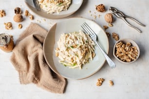 a white plate topped with pasta next to a bowl of nuts