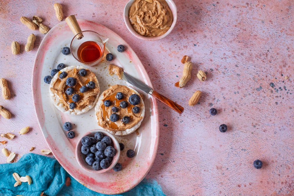 a white plate topped with blueberries and pancakes next to a bowl of peanut butter
