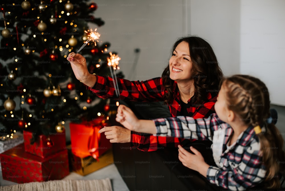 Una mujer y una niña sosteniendo bengalas frente a un árbol de Navidad