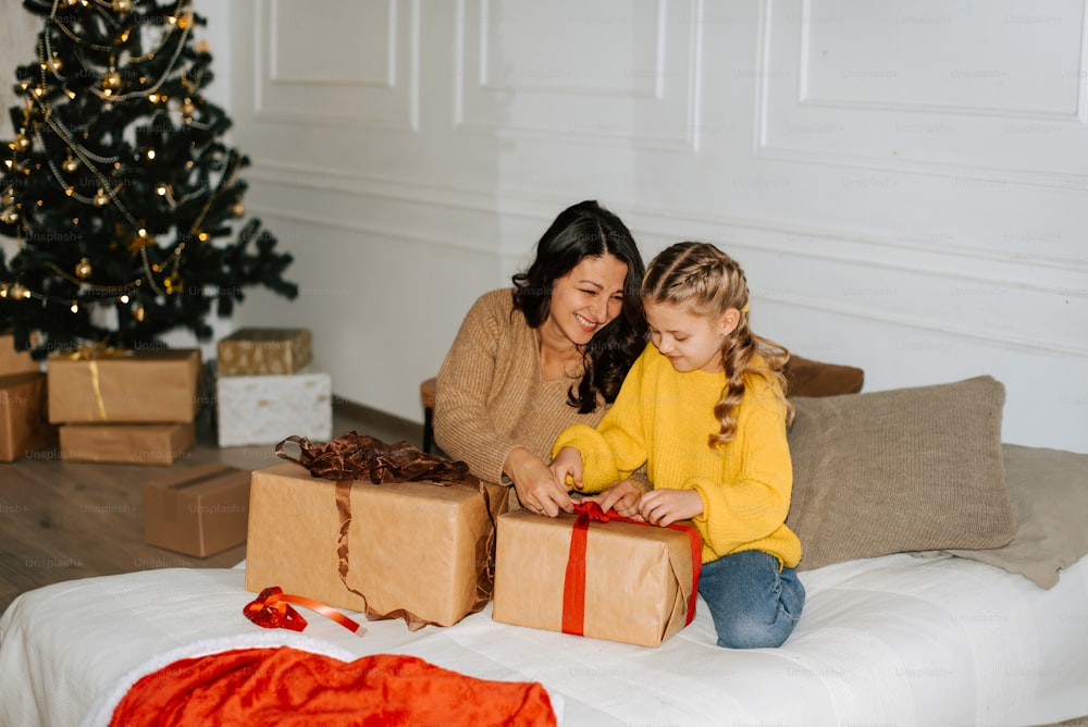 a woman and a little girl sitting on a bed with presents