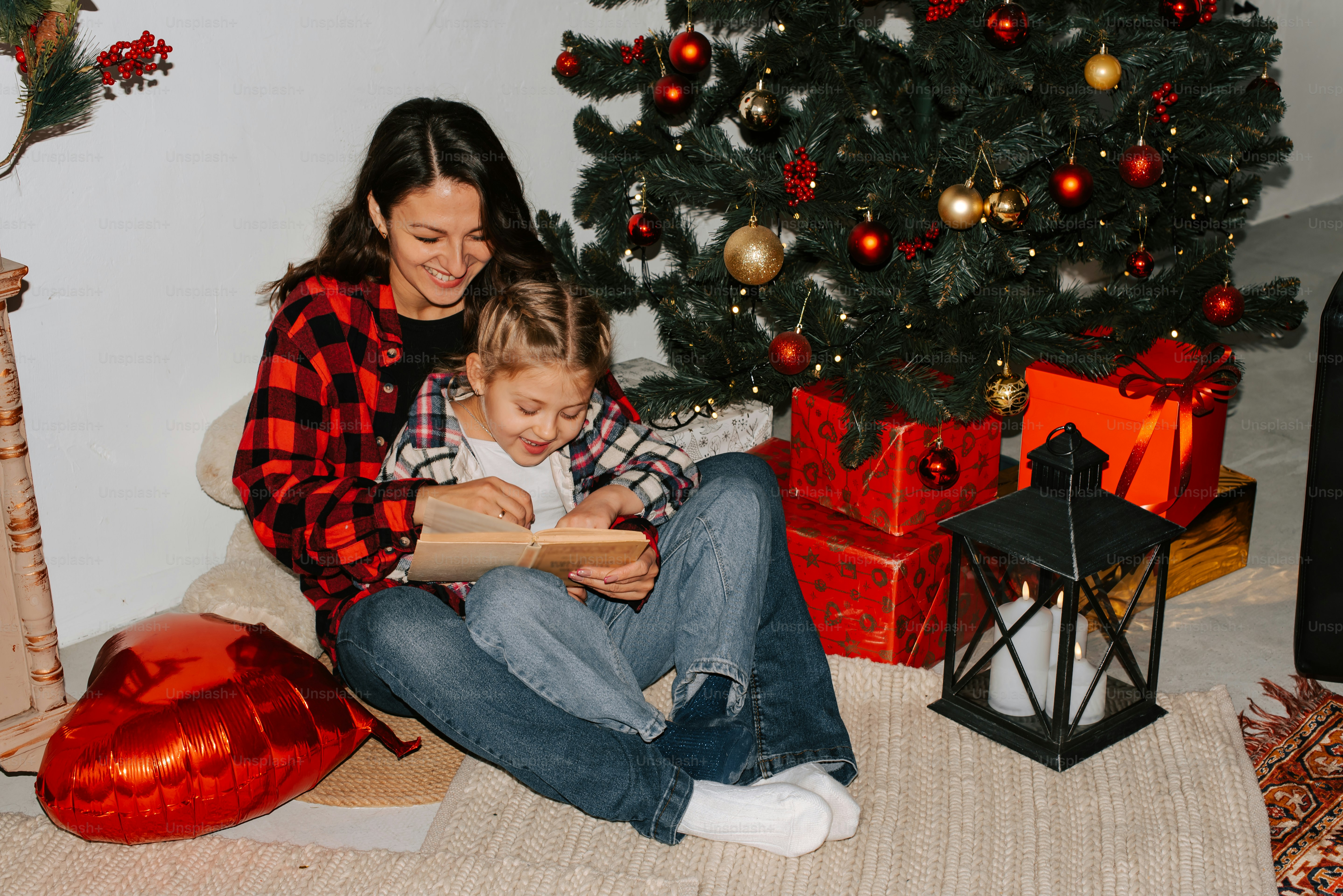 a woman reading a book to a child in front of a christmas tree