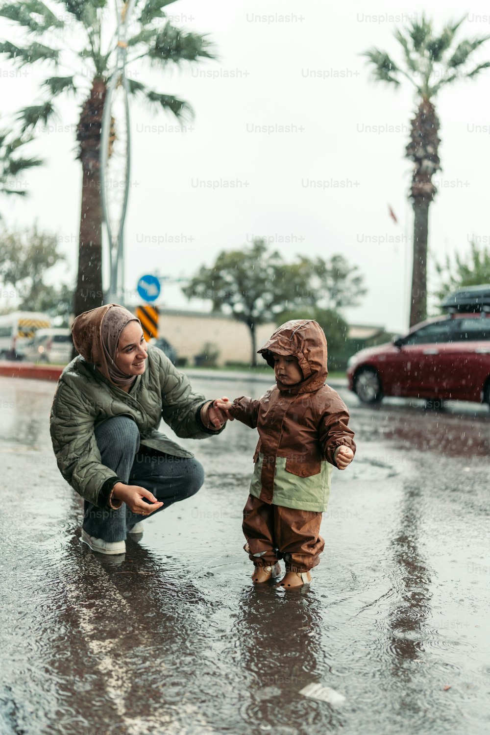 a woman kneeling down next to a child in the rain