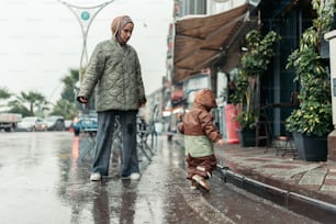 a woman and a child walking down a street in the rain