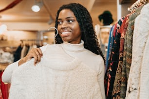 una mujer de pie frente a un perchero de suéteres