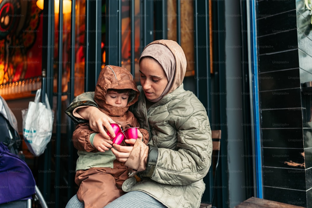 a woman and child sitting on a bench looking at a cell phone
