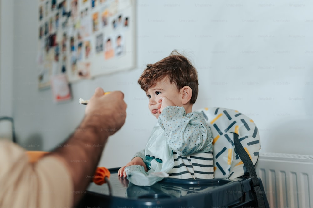 a young child sitting in a highchair while a man holds a toothbrush