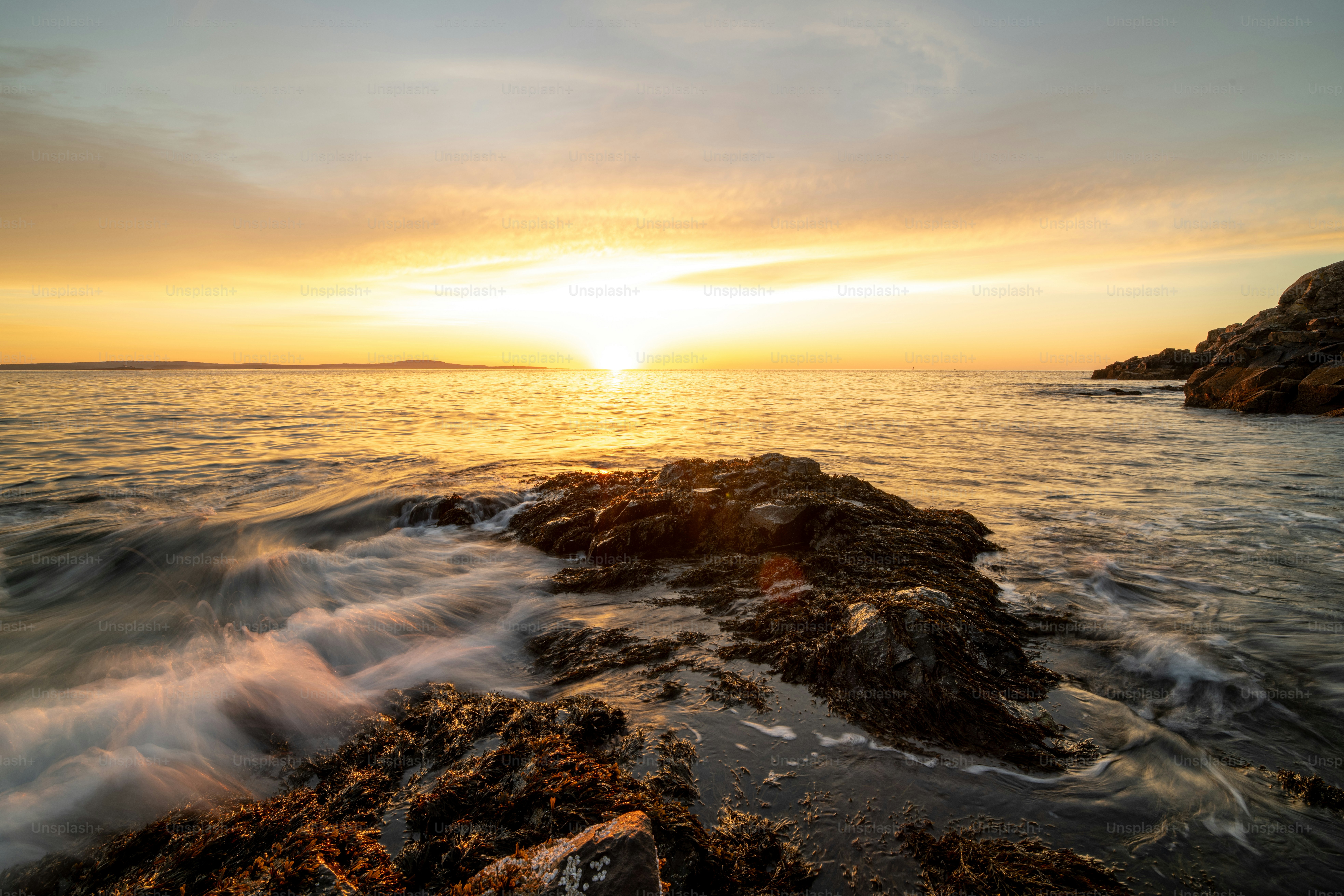the sun is setting over the water and rocks