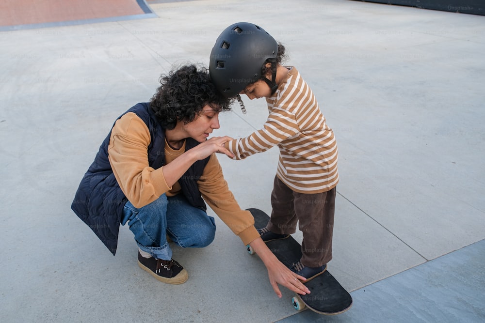 uma mulher ajoelhada ao lado de uma criança em um skate