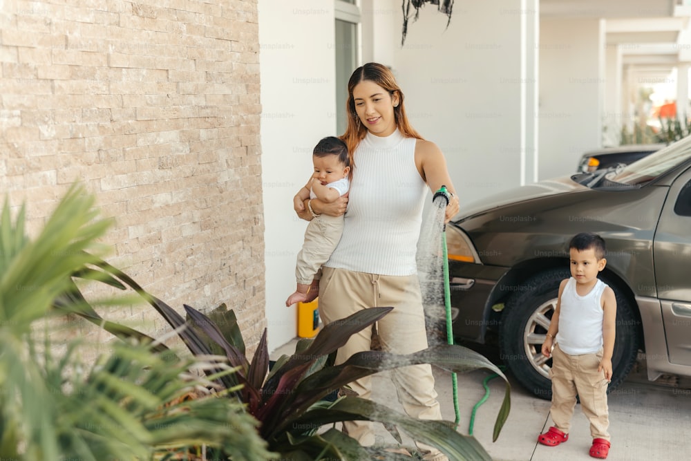 a woman holding a baby while standing next to a car