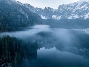 a lake surrounded by mountains covered in fog