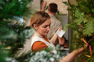 a man and a woman are working on a christmas tree