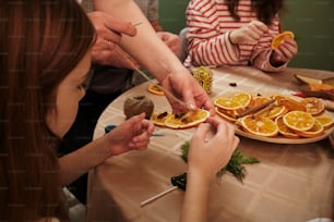 a group of people sitting around a table cutting orange slices